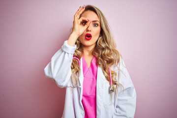 Young beautiful doctor woman using stethoscope over pink isolated background doing ok gesture shocked with surprised face, eye looking through fingers. Unbelieving expression.