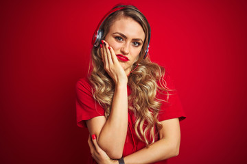 Young beautiful woman wearing headphones over red isolated background thinking looking tired and bored with depression problems with crossed arms.