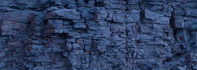 Rock cliff face background. Toned. Copy space for user text. Dangerous vertical wall with protruding crumbling layered stone blocks in quarry of wild stone. Abstract texture for stone mining industry