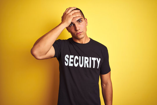 Young safeguard man with security t-shirt over yellow isolated background stressed with hand on head, shocked with shame and surprise face, angry and frustrated. Fear and upset for mistake.