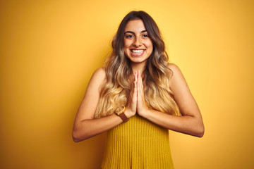 Fototapeta premium Young beautiful woman wearing t-shirt over yellow isolated background praying with hands together asking for forgiveness smiling confident.