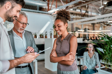 Good job! Young man is showing something on digital tabet to his collegaues while standing together in the modern office