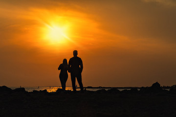 Fototapeta na wymiar silhouettes of man and woman on a dais stand with their backs and look at sea sunset