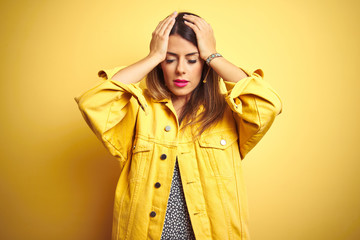 Young beautiful woman wearing denim jacket standing over yellow isolated background suffering from headache desperate and stressed because pain and migraine. Hands on head.