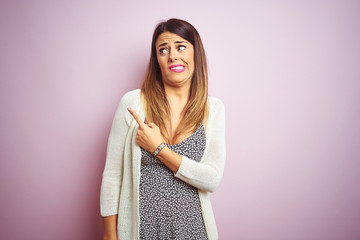 Young beautiful woman standing over pink isolated background Pointing aside worried and nervous...