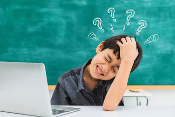 Asian confused school boy using laptop on black board background with tired and strain face and question mark sign.Creative education of kid student concept.