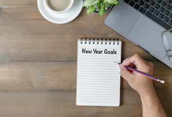 Hand man writing New year goals on note paper
