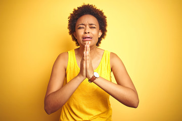 Beauitul african american woman wearing summer t-shirt over isolated yellow background begging and praying with hands together with hope expression on face very emotional and worried - obrazy, fototapety, plakaty