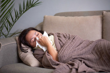Ill upset woman blowing running nose got flu caught cold sneezing in tissue sit on sofa, sick...