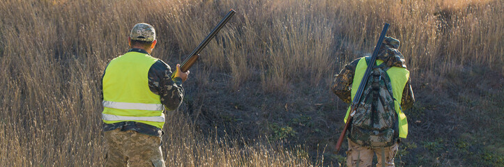 Silhouette of a hunter with a gun in the reeds against the sun, an ambush for ducks with dogs	