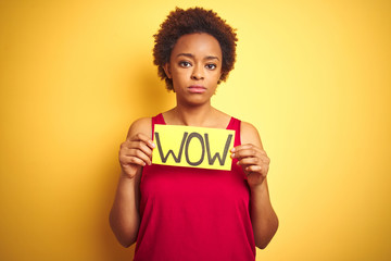 Young african american woman showing wow banner board over yellow isolated background with a confident expression on smart face thinking serious