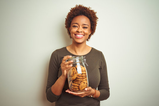 African american woman holding jar of chocolate chips cookies over isolated background with a happy face standing and smiling with a confident smile showing teeth