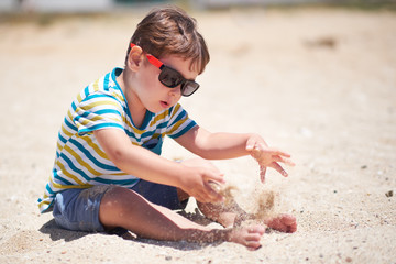 holiday, little boy three years old fun digging in the sand at the beach