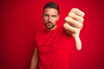 Young handsome man wearing casual t-shirt over red isolated background looking unhappy and angry...