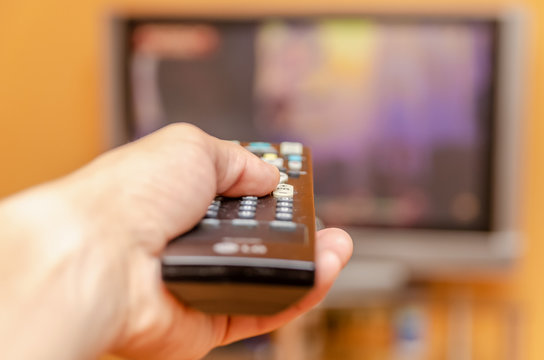 Man's hand holding a tv remote control, pressing a button while pointing at a flat screen tv.