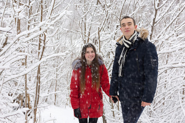 The guy and the girl have a rest in the winter woods. Husband and wife in the snow. Young couple walking in winter park	