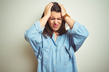 Young beautiful brunette woman wearing casual blue denim shirt over isolated background suffering from headache desperate and stressed because pain and migraine. Hands on head.