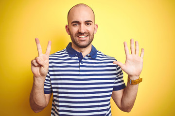 Fototapeta premium Young bald man with beard wearing casual striped blue t-shirt over yellow isolated background showing and pointing up with fingers number seven while smiling confident and happy.