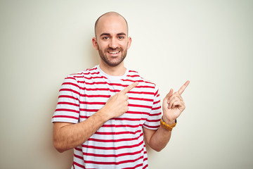 Fototapeta premium Young bald man with beard wearing casual striped red t-shirt over white isolated background smiling and looking at the camera pointing with two hands and fingers to the side.