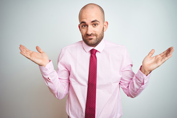 Young business man wearing pink tie over isolated background clueless and confused expression with arms and hands raised. Doubt concept.