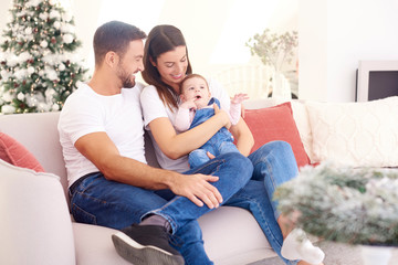 Lovely family with their baby girl relaxing on sofa at home during Christmas