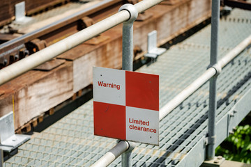 Isolated view of a Limited Clearance sign on a railway bridge. Warning pedestrians to keep away of the tract when a train passes, to avoid a possible collision.