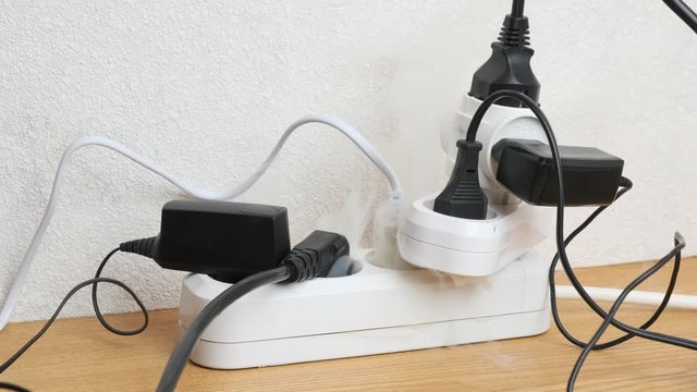 power strip smoking from overload by electrical appliances on table in room in close-up. concept of occurrence of fire.