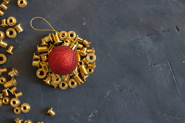 Round form made of gold pop rivet nuts ond lochnuts with red christmas ball on it on black tectured chalk board. Horizontal copy space. Fasteners, screws and details. Top view. New year concept.