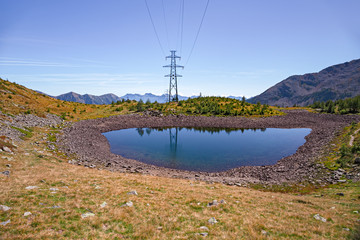 Panoramic view of a mountain lake on a sunny autumn day. In the background a high voltage pylon.
