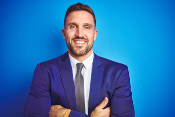 Close up picture of young handsome business man over blue isolated background happy face smiling with crossed arms looking at the camera. Positive person.