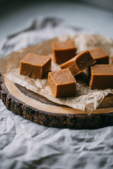 Fresh caramel fudge candies on a wooden plate with copy space in marble background
