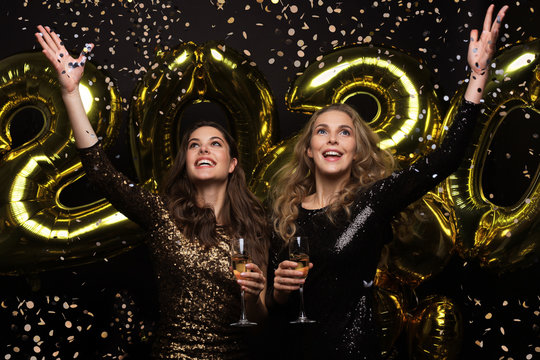 Happy gorgeous girls in stylish sexy party dresses holding gold 2020 balloons, having fun at New Year's Eve Party.