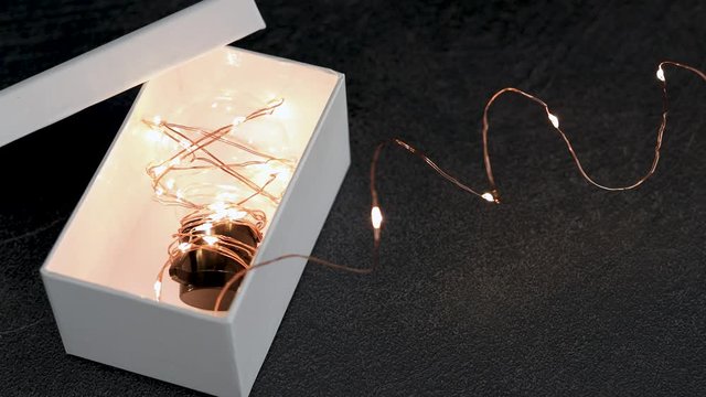 thinking outside the box, idea lightbulb wrapped up in string lights going on and off from open box