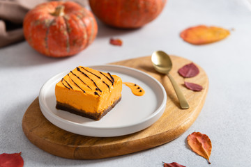 Pumpkin pie, decorated with chocolate on white plate, pumpkin and autumn leaves on white background. Confectionery, menu, banner. Autumn dessert.