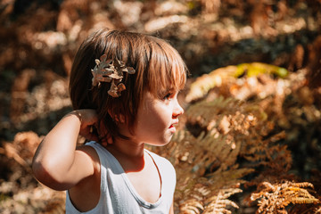 Little caucasian baby girl squatting in the forest among ferns