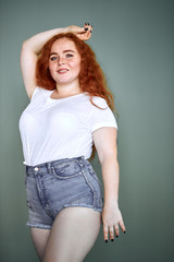 Young caucasian girl with red hair wearing white t-shirt and shorts, posing, look at camera. Red...