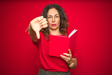 Middle age senior woman reading a book over red isolated background with angry face, negative sign showing dislike with thumbs down, rejection concept