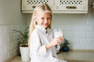 Happy blonde long hair little girl drinking milk in kitchen, healthy lifestyle