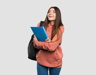 Young student woman holding notebooks looking up while smiling over isolated grey background