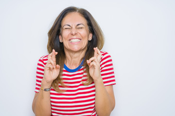 Middle age senior woman standing over white isolated background gesturing finger crossed smiling with hope and eyes closed. Luck and superstitious concept.