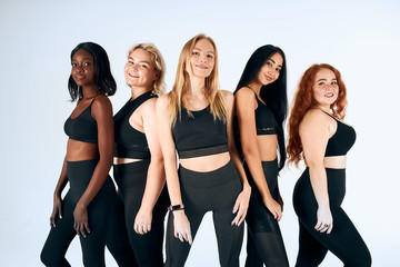 Young and positive girls of different nations stand smiling, look at camera isolated in white studio background