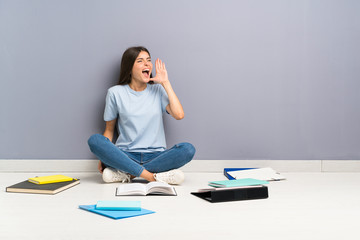 Young student woman with many books on the floor shouting with mouth wide open