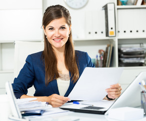 Smiling woman working with papers and laptop in office