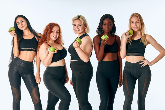 Young attractive girls holding green apple posing in studio, white background. Promotion of healthy lifestyle - Powered by Adobe