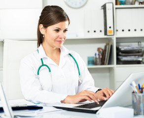Cheetful woman doctor sitting at workplace with computer in her office