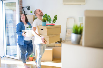 Young couple moving to a new home, smiling happy holding cardboard boxes