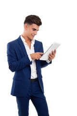 Naklejka na ściany i meble young smiling businessman using a white tablet mobile. He is wearing a blue jacket suit and a white shirt. He is in a photo studio.