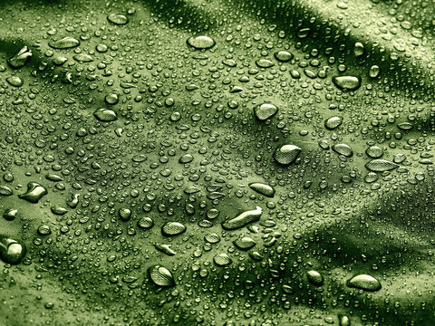 Fiber waterproof fabric with rain water droplets. Green background.