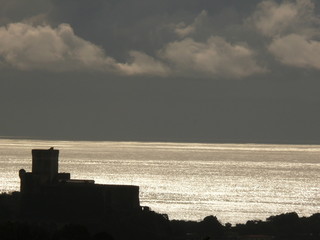 Fototapeta premium Silhouette of the castle of Lerici at sunset. Sky with clouds and sea of gold color.