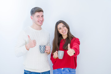 Beautiful young couple over white isolated background drinking a cup of coffee happy with big smile doing ok sign, thumb up with fingers, excellent sign